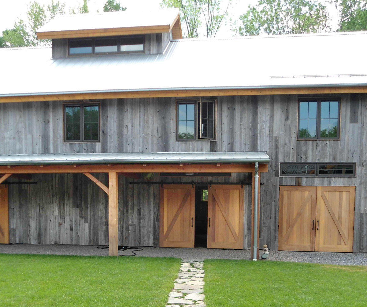 Flat track cedar doors allow access under the overhang of a timber frame barn in Upstate, NY.