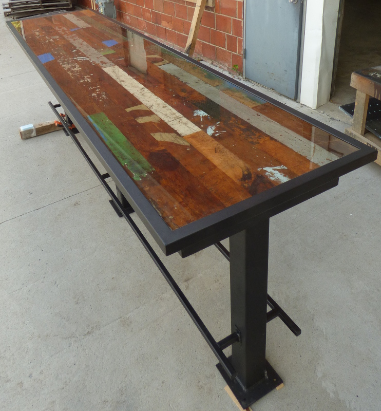 Headed for its new life as a bar height community table, this creation has intentionally selected planks from original Foundry Maple flooring with a resin pour finish atop a powder coated custom steel base.