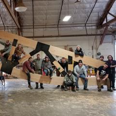 The New Energy Works timber framing and fabrication team sits amongst a massive 60-foot glulam truss.